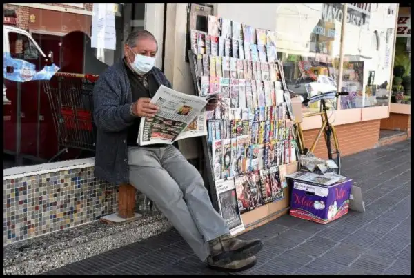 En el quiosco de diarios y revistas, leyendo con barbijo.